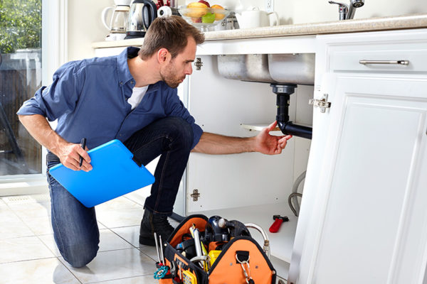 Plumber checking pipes under kitchen sink.